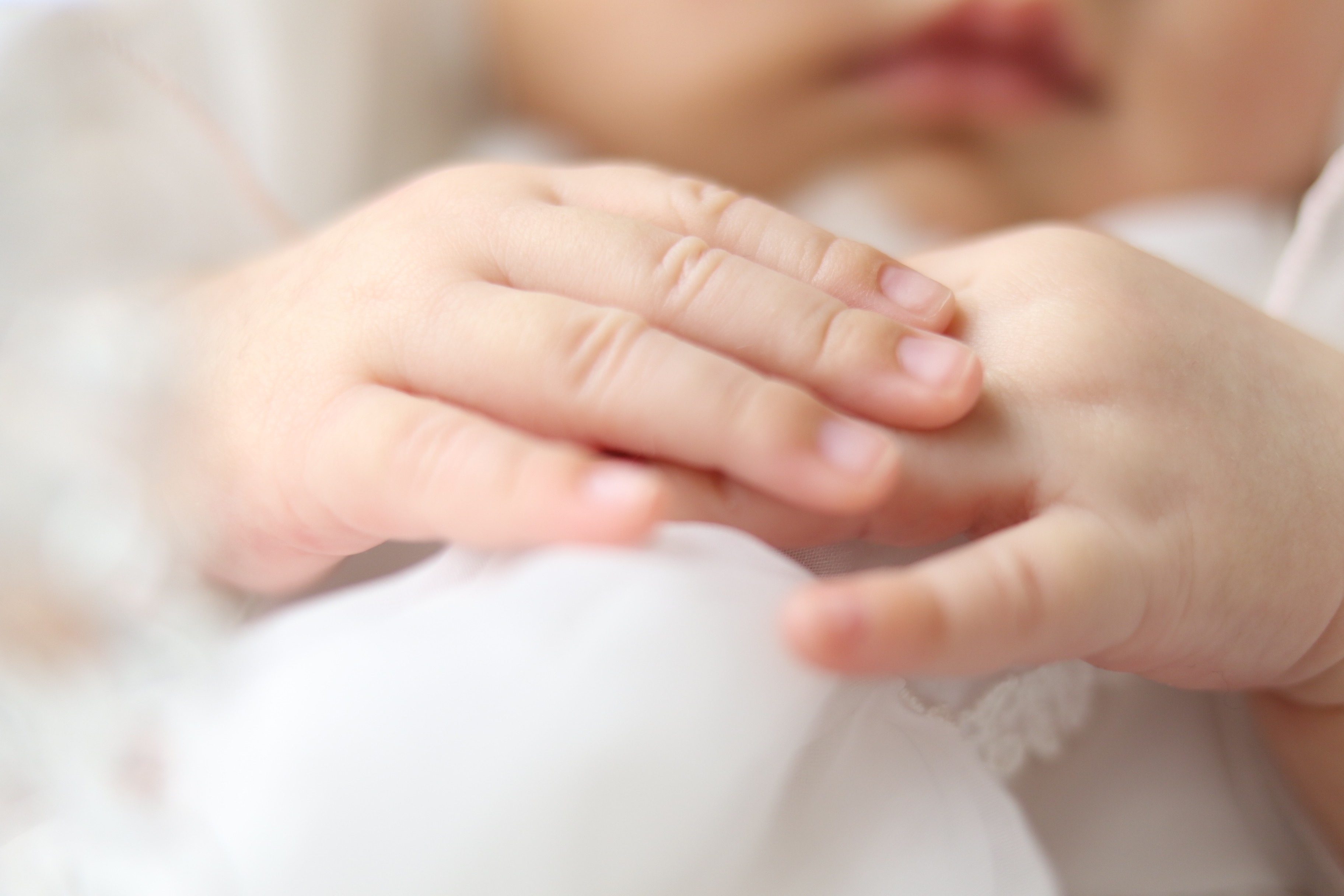 窓辺のやわらかな光の中で、赤ちゃんの手にそっと寄り添う手