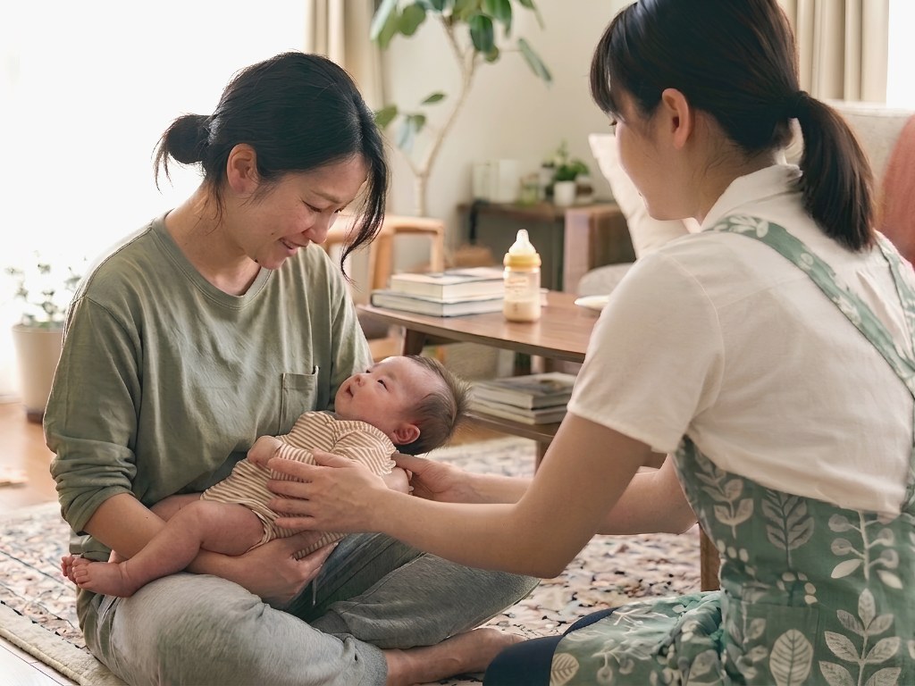 ご自宅で助産師が赤ちゃんを抱くお母さんに寄り添う訪問ケアの様子